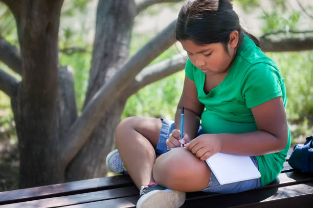 A homeschooled child sitting in an outdoor garden in a relaxed pose, while solving or learning elementary school level subjects. stock photo