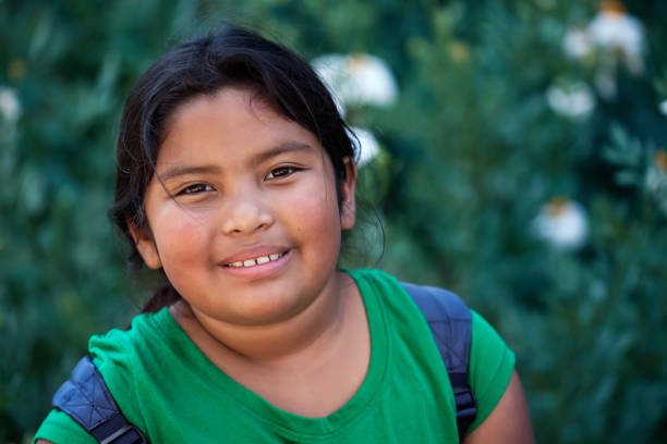 istock Cute elementary student with backpack in front of green flowers with a positive attitude and natural look. 1153714908