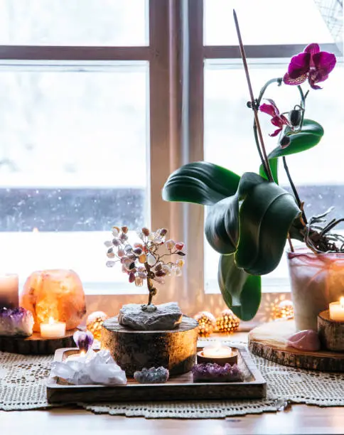 Photo of Feng Shui nature theme altar at home table and on window sill. Earth element( rock crystal clusters), wood element( wood discs), fire element( candles), rock salt candle holder. Positive home energy.