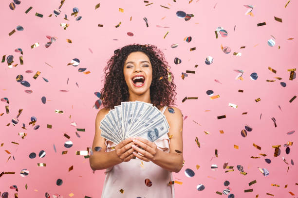 black afro american girl won money. happy young woman holding dollar currency satisfied isolated over pink background with confetti. - smiling casino human hand beautiful imagens e fotografias de stock