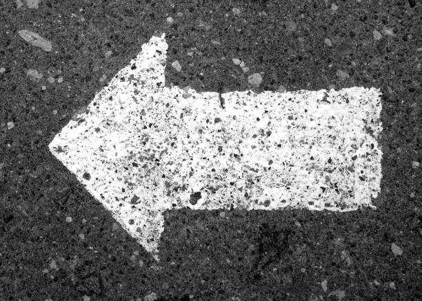 Left pointing arrow on asphalt in black and white. Signs and symbols.