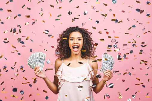 La chica afroamericana negra ganó dinero. Feliz mujer joven sosteniendo moneda de dólar satisfecho aislado sobre fondo rosado con confeti. photo