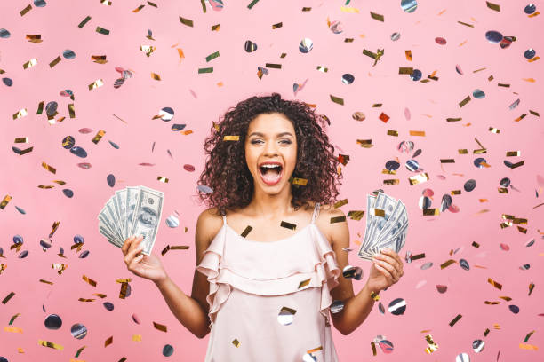la chica afroamericana negra ganó dinero. feliz mujer joven sosteniendo moneda de dólar satisfecho aislado sobre fondo rosado con confeti. - jackpot fotografías e imágenes de stock