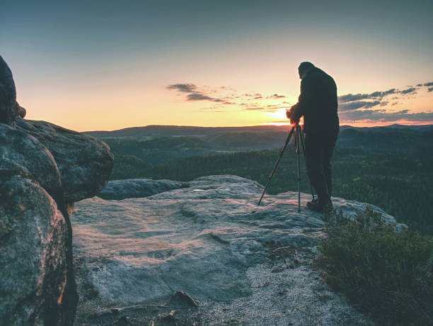 istock Photographer check display of camera on tripod. Man stay on cliff 1153720825