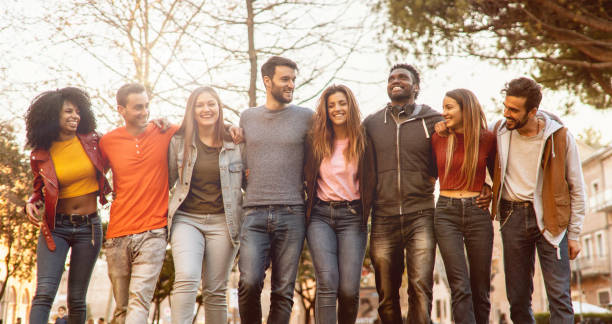 Group of multiracial young people students arms around shoulders together in a park stock photo