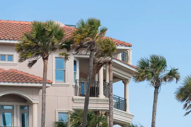 Closeup of colorful villa house or home with palm trees red tiles tiled roof against blue sky in typical Florida panhandle community