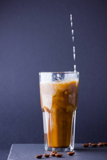 istock Iced coffee with milk on a dark background. Summer drink with caffeine on the slate board. Latte in a glass cup and coffee beans. Copy space 1153733366