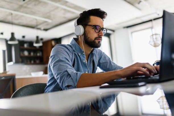 istock Young modern bearded man working with laptop computer indoors 1153736957