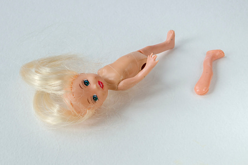 Broken doll with torn off leg and torn hair on a light background