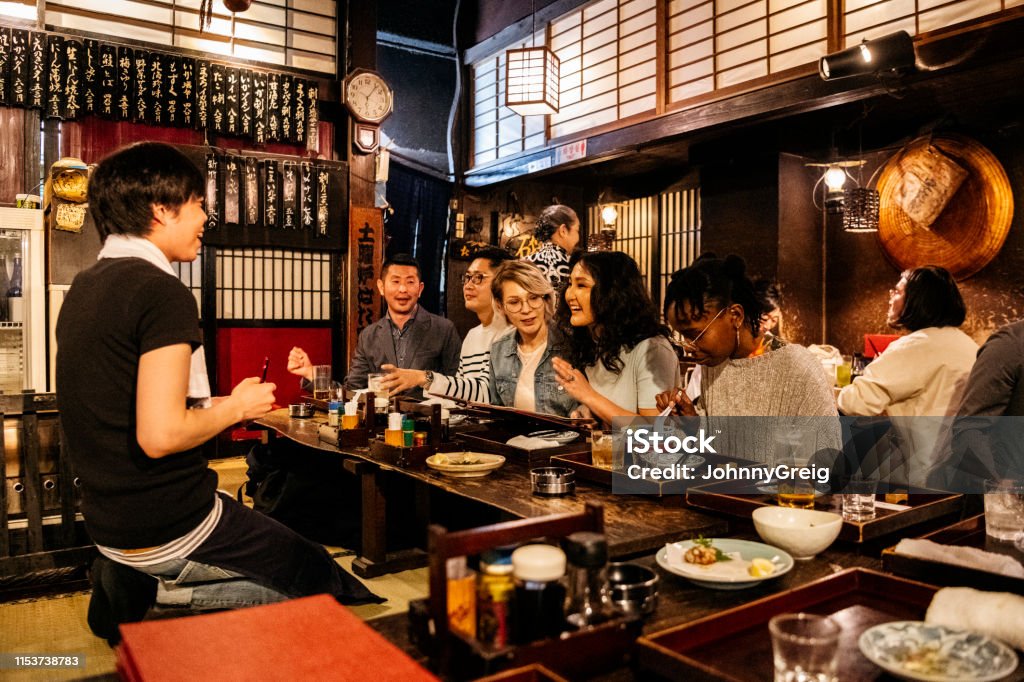 Group of friends ordering food in Japanese Izakaya Waiter taking food order from happy group of friends, night out, drinking, eating Japan Stock Photo