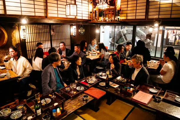 High angle view of work friends and colleagues sitting at corner of bar in traditional Izakaya, nightlife, relaxation, socialising