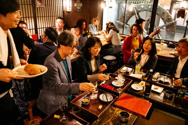 Friends and colleagues enjoying food and drink after work in busy Japanese Izakaya, relaxation, team building, friendship