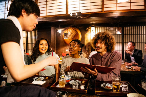 Waiter taking food order from friends in Japanese restaurant Hipster couple ordering food from menu in Japanese Izakaya, nightlife, decisions, cheerful central asian ethnicity photos stock pictures, royalty-free photos & images