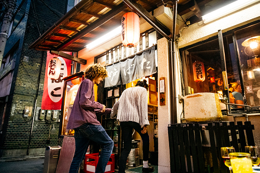 Hipster young man and woman walking into Japanese bar with lanterns, nightlife, date, food and drink
