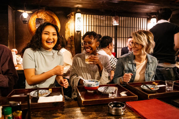 Three female friends relaxing after work in Japanese Izakaya Young women laughing on night out, food and drink, bonding, carefree central asian ethnicity stock pictures, royalty-free photos & images