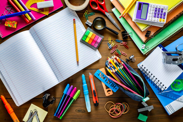 Overhead shot of stationery on wood desk with paper notepad and frame of school office supplies Back to school themes. Overhead shot of stationery on wood desk with paper notepad and frame of school office supplies stapled paper stock pictures, royalty-free photos & images