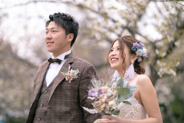 istock Happy bride and groom standing together under cherry blossoms 1153751195
