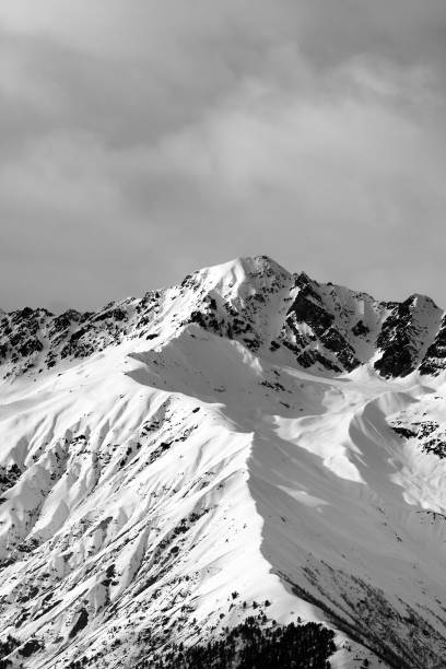 istock Black and white view on snow sunlit mountain and cloudy sky at winter evening 1153753870