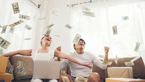 Happy couple smiling successful sitting under money rain. Business online concept stock photo