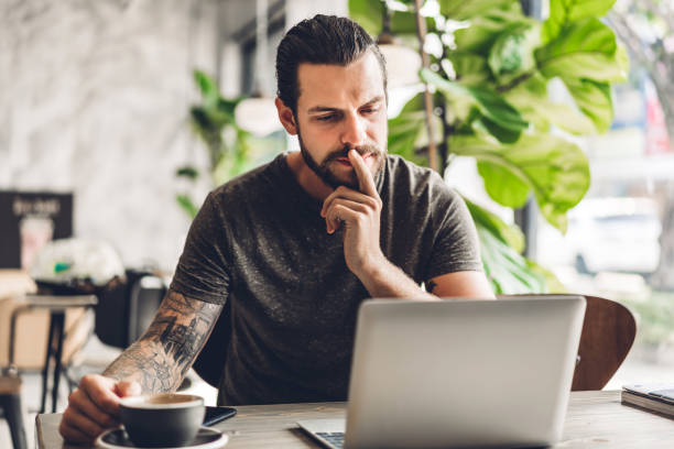 istock Handsome bearded hipster man use and looking at laptop computer with coffee at table in cafe.Communication and technology concept 1153776431
