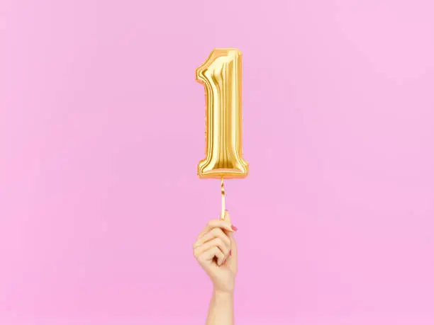 One year birthday. Female hand holding Number 1 foil balloon. One-year anniversary background. 3d rendering