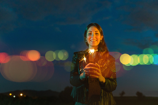 Young woman holding a sparkler at dusk