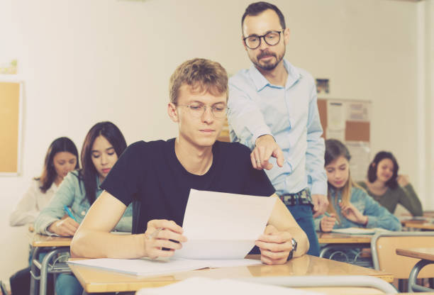 istock Schoolboy is writing answer the question on paper and teacher explaining it 1153796025