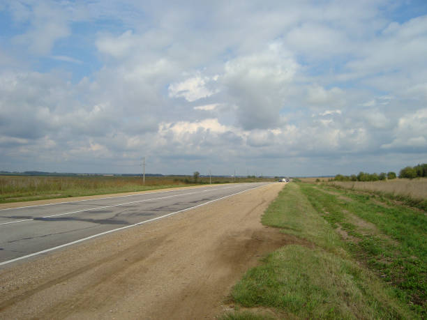 istock Direct asphalt road through the countryside under the sky, on which the clouds float. 1153799931
