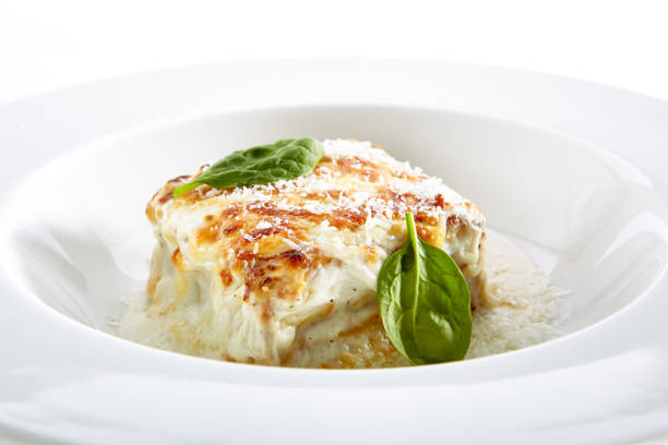 Close-up portrait of portion of tasty lasagna decorated with some lettuce served on shiny plate. Restaurant delicacy concept. Isolated on white background