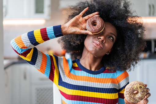 Afro woman holding donuts in front her face