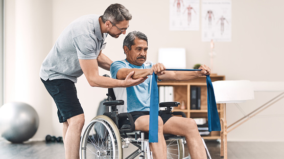 Shot of a senior man in a wheelchair exercising with a resistance band along side his physiotherapist