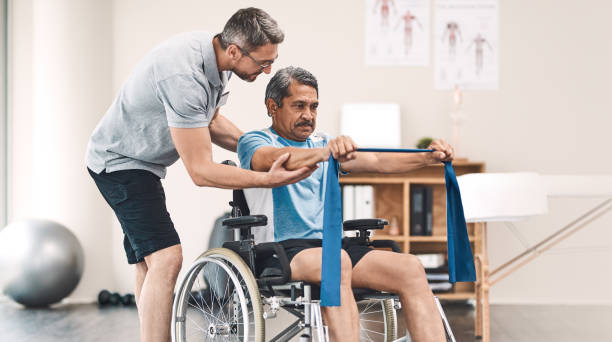 Taking it up a notch day by day Shot of a senior man in a wheelchair exercising with a resistance band along side his physiotherapist paraplegic stock pictures, royalty-free photos & images