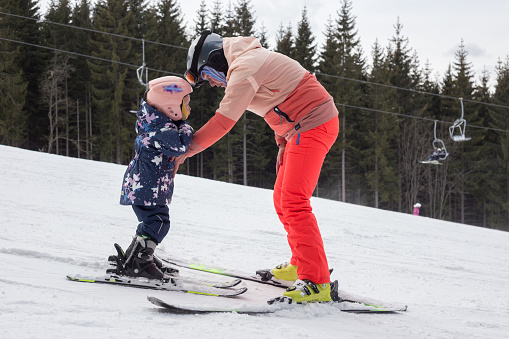 Mother teaches child to ski. The child moves down the ski slope for the first time in his life.