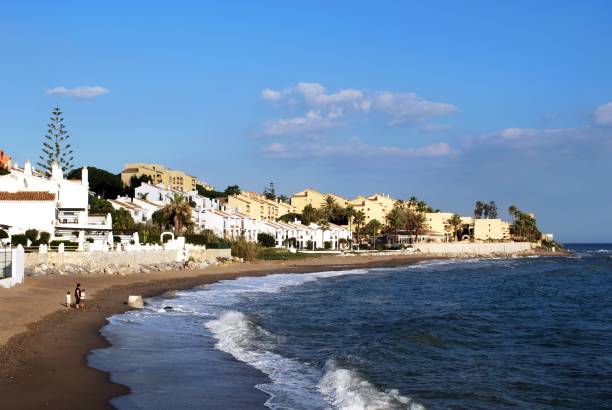 View along the beach towards apartments with a mother and children on the shoreline, Sitio de Calahonda, Costa del Sol, Malaga Province, Andalucia, Spain, Europe.