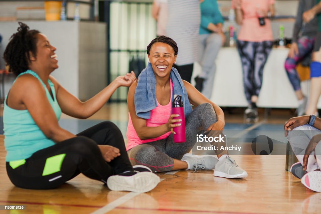 Friends sitting on the floor and talking after dance class while drinking water Gym Stock Photo