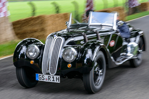 BMW 328 classic 1930s sports car driving at high speed on a country road