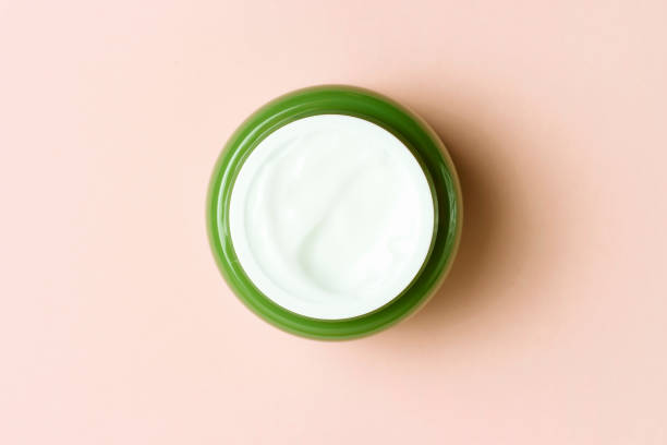 istock Green jar with white cream on a pink background, close-up, top view 1153830974