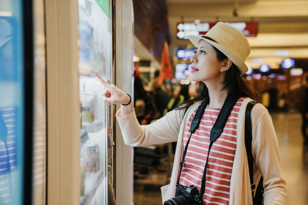photographer using modern vending machine asian travel woman photographer using modern vending machine in airport while waiting for plane flight in departure gate. young girl right hand finger pointing choosing snack drinks to buy. vending machine stock pictures, royalty-free photos & images