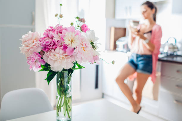 istock Modern kitchen decorated with pink peonies. Woman having coffee and relaxing using phone. Interior design. 1153839690