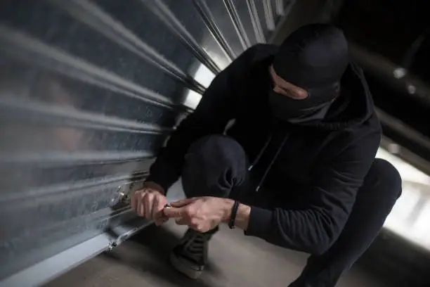 Burglar trying to rob a garage. Unrecognizable Caucasian male wearing a balaclava.