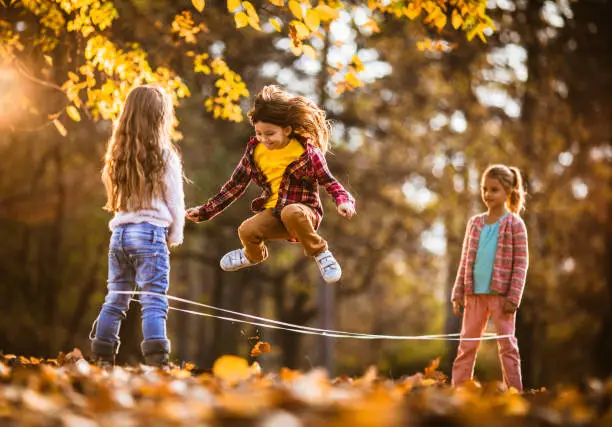 Happy little girls having fun while skipping rubber band during autumn day at the park.