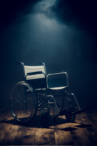Lonely empty wheelchair in dark room. Medical equipment for disabled patient.