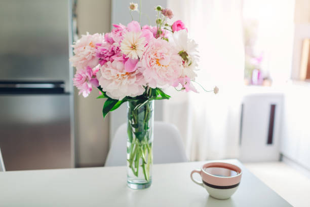 istock Pink peonies with tea on table. Modern kitchen design. Interior of white and silver kitchen decorated with flowers. 1153861399