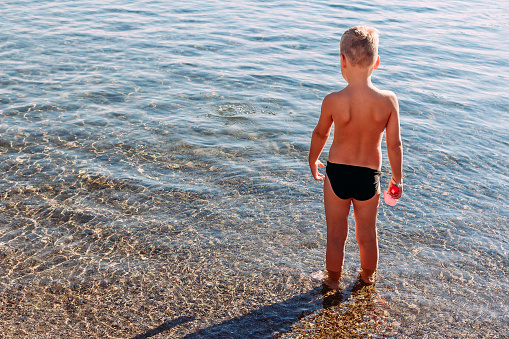 seven-year-old tanned child stands with his back to the camera on the sea in the summer. children and sea.