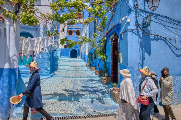 People walking in a street of Chefchaouen, Morocco Chefchaouen, Morocco - May 3, 2019: Traditional scene with people walking through one of the beautiful streets with blue painted facades of the village of Chefchaouen, in northern Morocco chefchaouen stock pictures, royalty-free photos & images