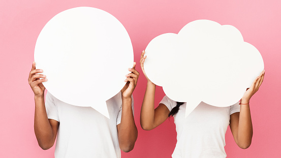 Couple holding empty speech bubbles, closing their faces over pink background