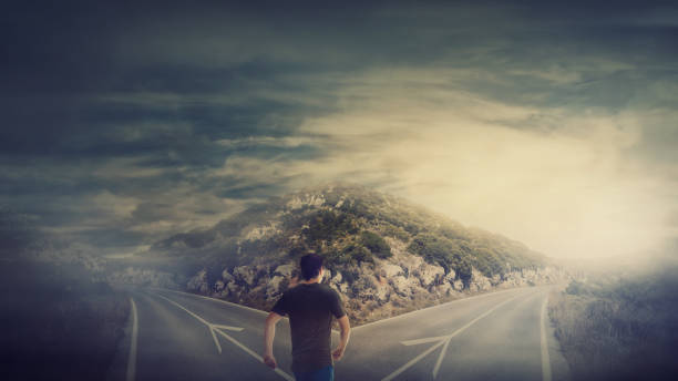 istock Rear view man walking in front of crossroad as road is split in two different ways. Choosing the correct path between left and right, failure or success. Difficult decision concept 1153885725
