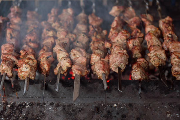 Traditional Caucasian BBQ shashlik grilled meat on sticks being cooked on open fire with smoke, close up view.