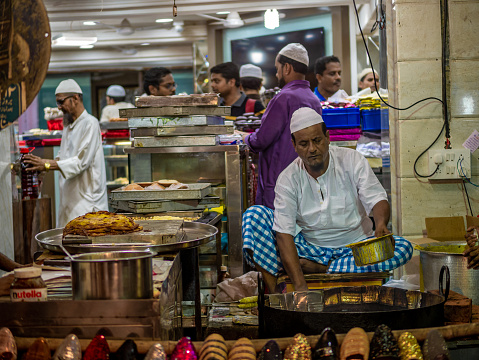 Mumbai, India - May 11, 2019 : Muslim male vendors cooking selling halal foods and snacks fried pancake Malpuas from roadside stall at night market in holy month of Ramadan Ramazan at Bhendi Bazar