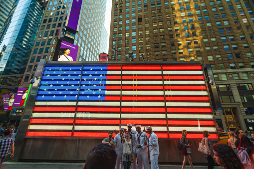 Group of People taking Photos on Broadway. Neon American Flag Light. Times Square, New York City, May 27, 2019